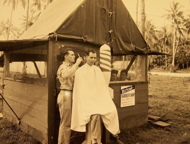 Looking for a trim on a South Pacific island? Look for the Warhawk Barber Shop with its barber pole made of a bomb shell. (NARA)