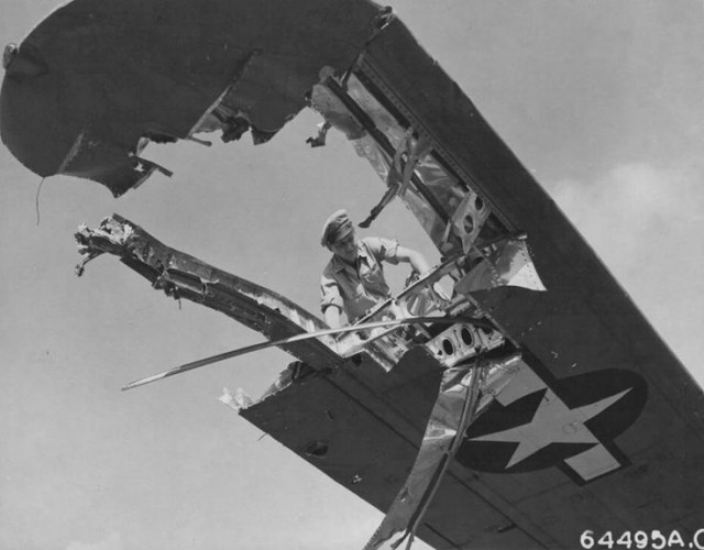 Crew member examines wing of a Consolidated B-24 “Liberator” which was badly-damaged during pre-invasion raid over Iwo Jima. Marianas Islands
