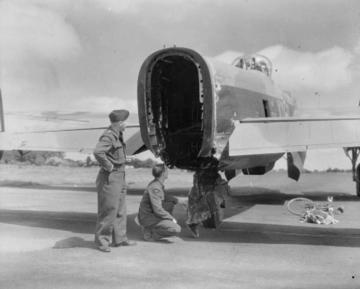 Two crew members from an Avro Lancaster B Mark II examine the rear of their aircraft, where the rear turret, along with its unfortunate gunner, was sheared off by bombs dropped from above.