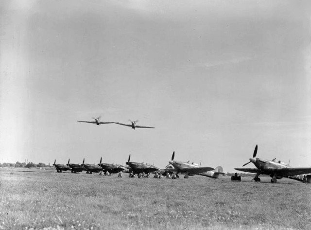 Two Royal Air Force Hawker Hurricane Mark IIs of No. 43 Squadron RAF make a low level pass over other aircraft of the Squadron, lined up at Tangmere, Sussex (UK)